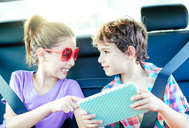 Deux enfants avec une tablette numérique, sur la banquette arrière d'une voiture.
